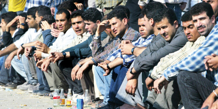 Striking Palestinian workers sit on the road near the Israeli industrial zone at the Erez Crossing, northern Gaza Strip, Wednesday, April 14, 2004. The industrial zone workers are holding a three day strike to protest security delays by Israeli authorities. (AP Photo/Kevin Frayer)