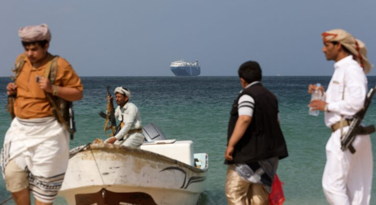 يمنيون يحملون أسلحة وفي الخلفية سفينة احتجزها الحوثيون - رويترز