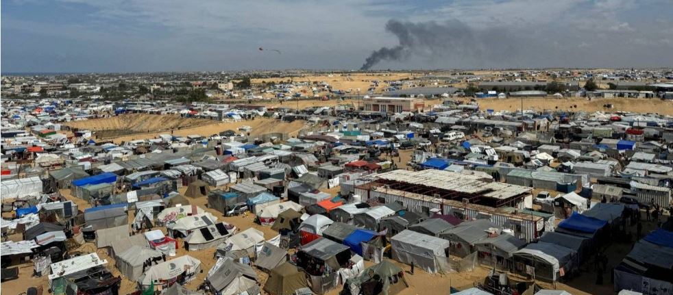 مخيم للنازحين برفح جنوب غزة وفي الخلفية يتصاعد الدخان بمدينة خان يونس